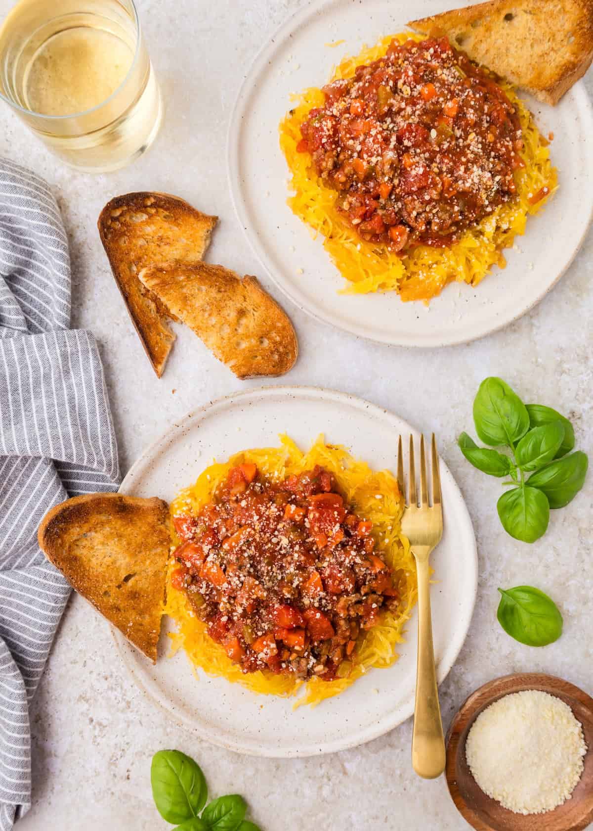 Two plates of spaghetti squash bolognese with toast, cheese, basil, and a refreshing drink.