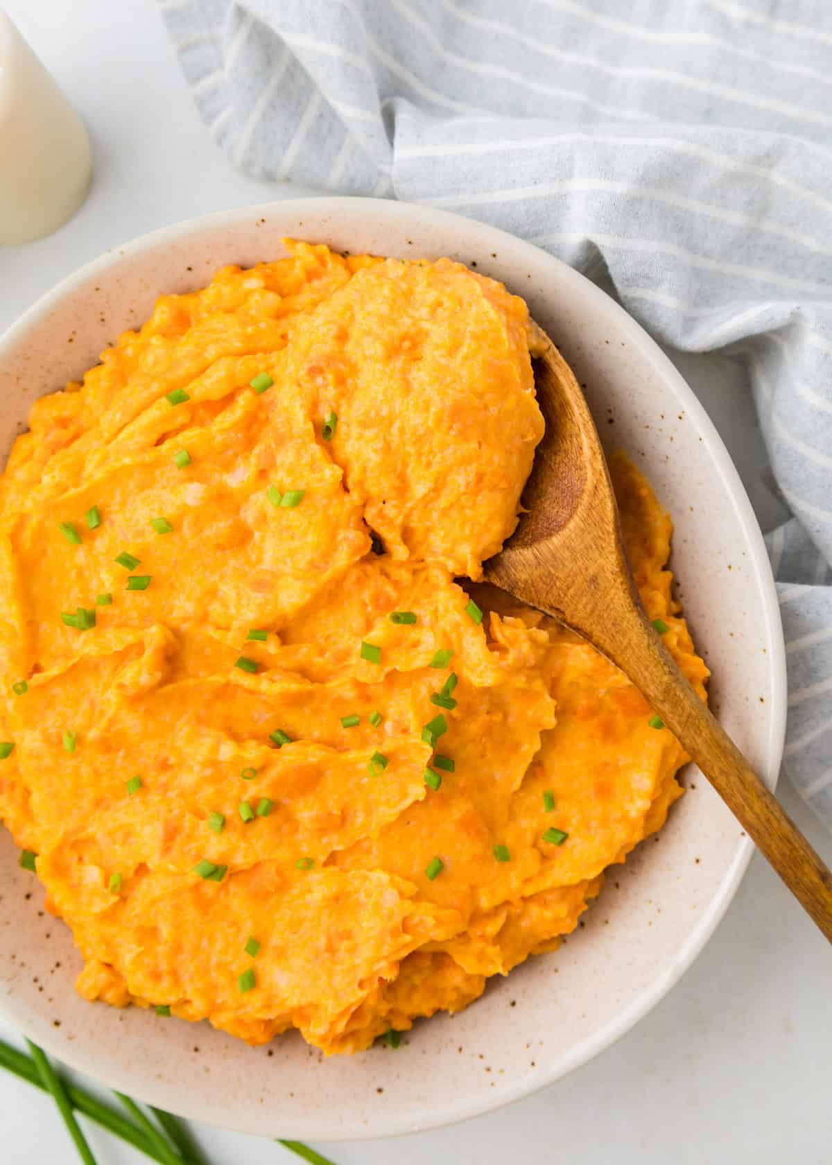 Carrot Mashed Potatoes in serving bowl with wooden spoon.