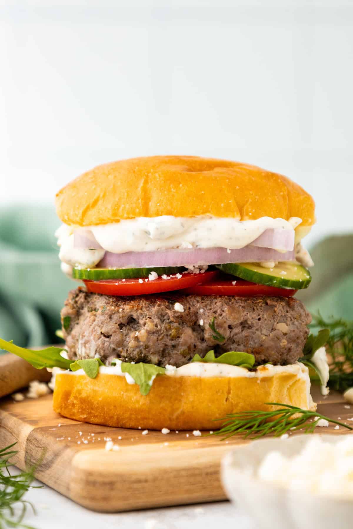 A lamb burger with lettuce, tomato, cucumber, onion, and sauce on a wooden board.