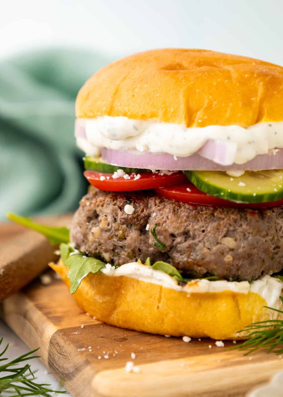 A juicy lamb burger with lettuce, tomato, onion, cucumber, and sauce on a wooden board.