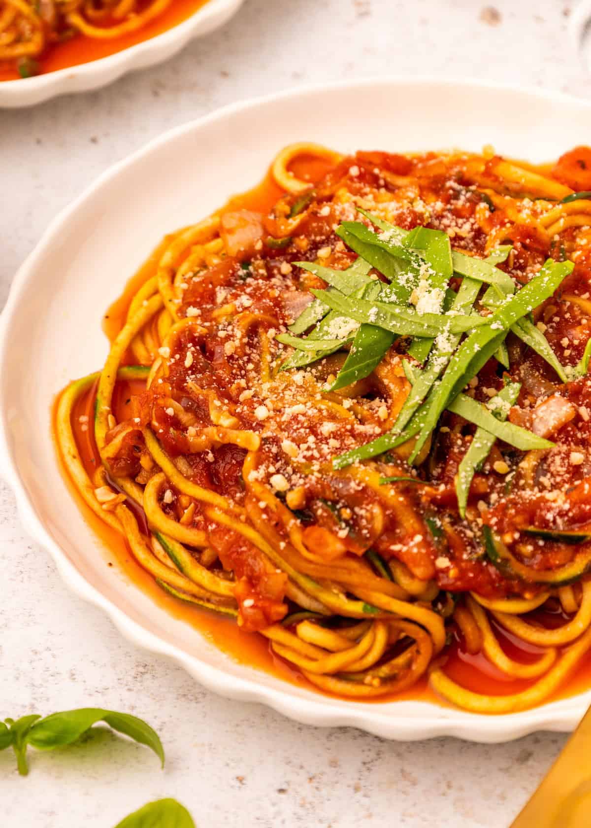 A plate of Zucchini Noodle Spaghetti with tomato sauce, grated cheese, and fresh basil.
