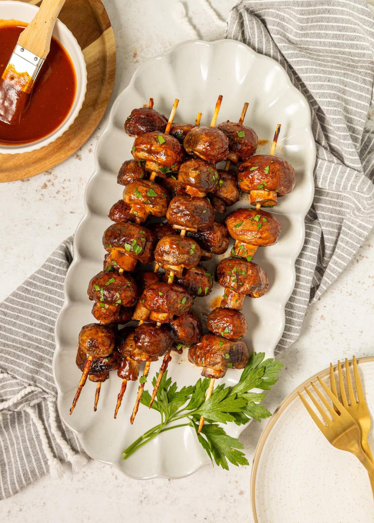 BBQ Mushrooms skewers with herbs on a white platter, served with tangy barbecue sauce.