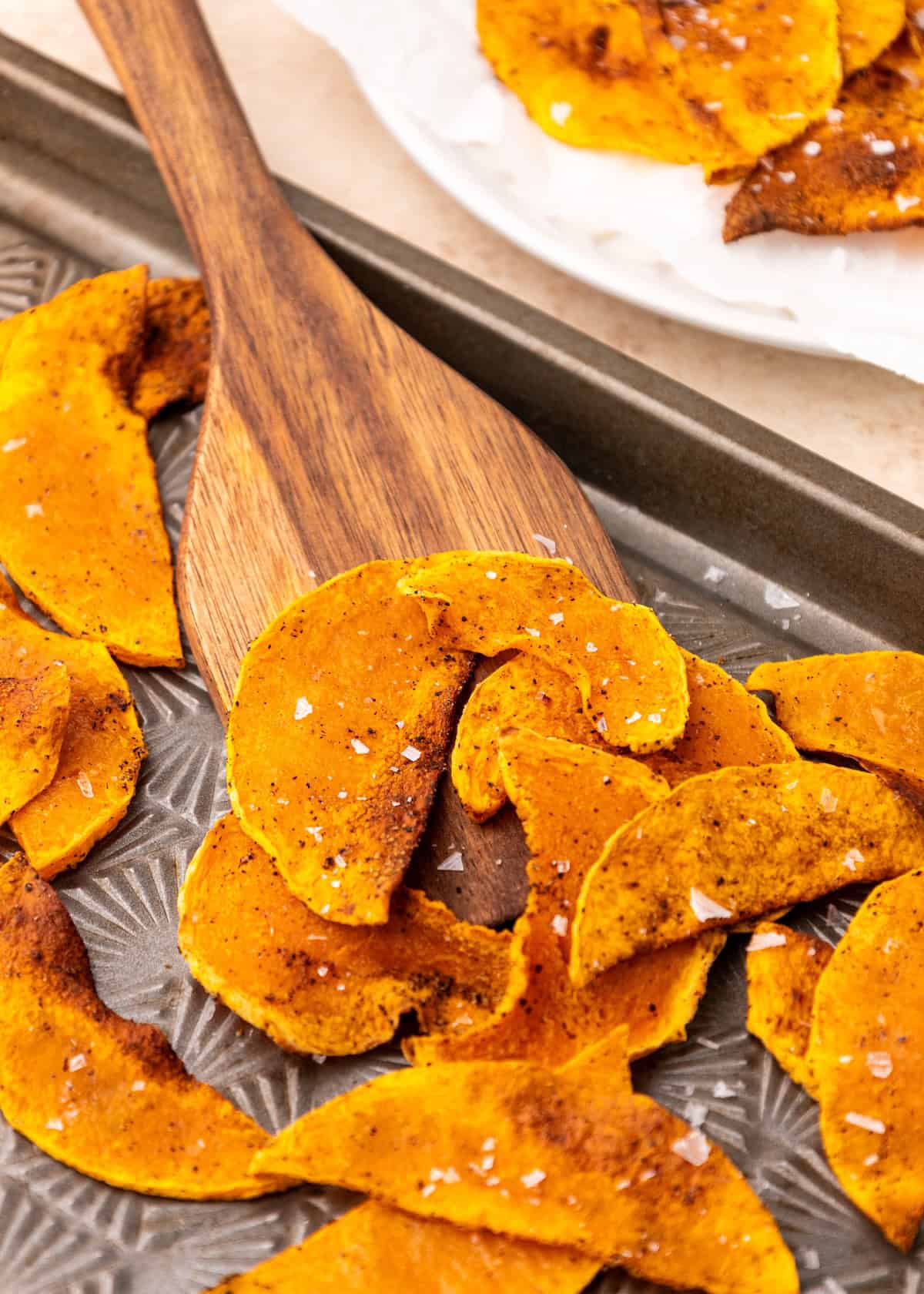 Butternut Squash Chips on a tray with a wooden spatula, sprinkled with sea salt.