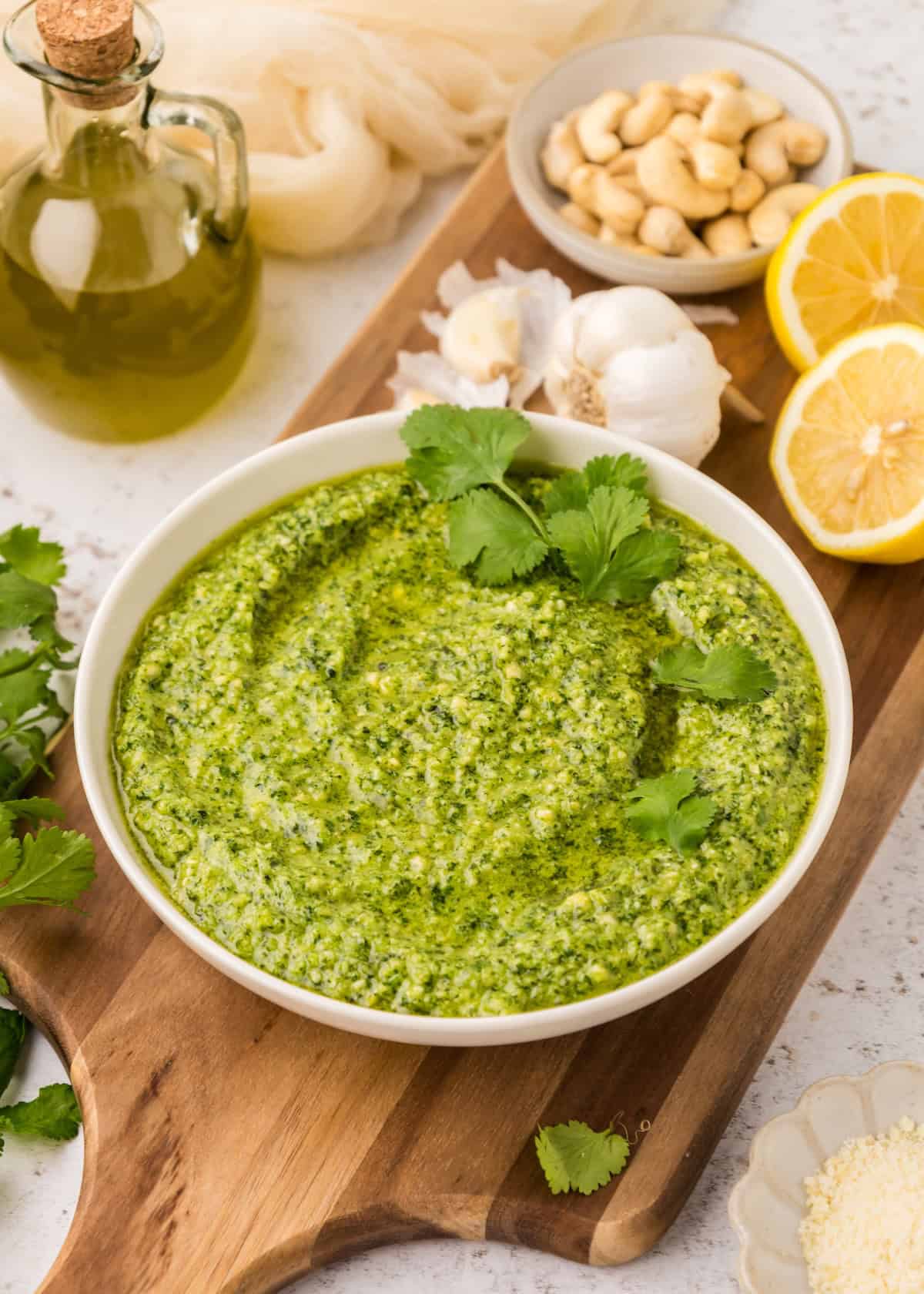 Bowl of cilantro pesto with garlic, lemon, cashews, and olive oil on a wooden board.