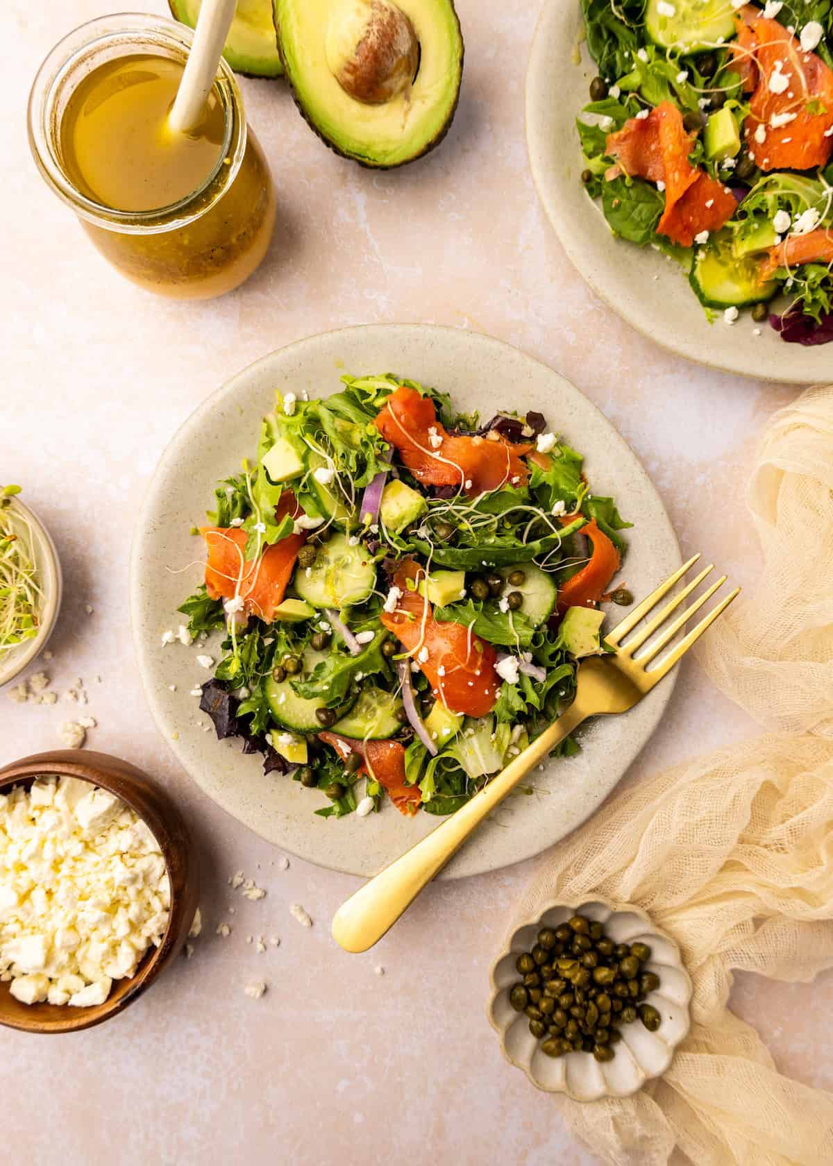 Smoked Salmon Salad with greens, cucumber, capers, sprouts, and a fork on the plate.