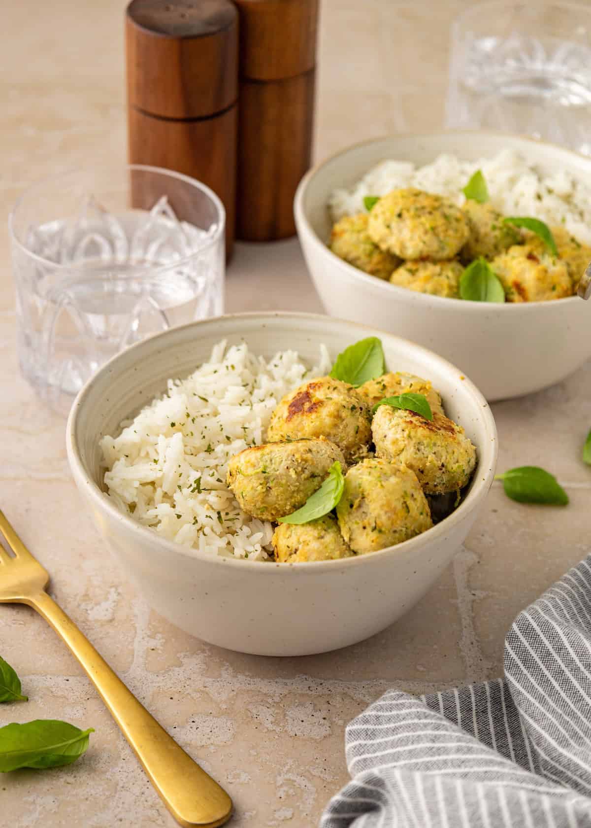 Two bowls of rice topped with chicken meatballs and basil leaves for a fresh, savory meal.