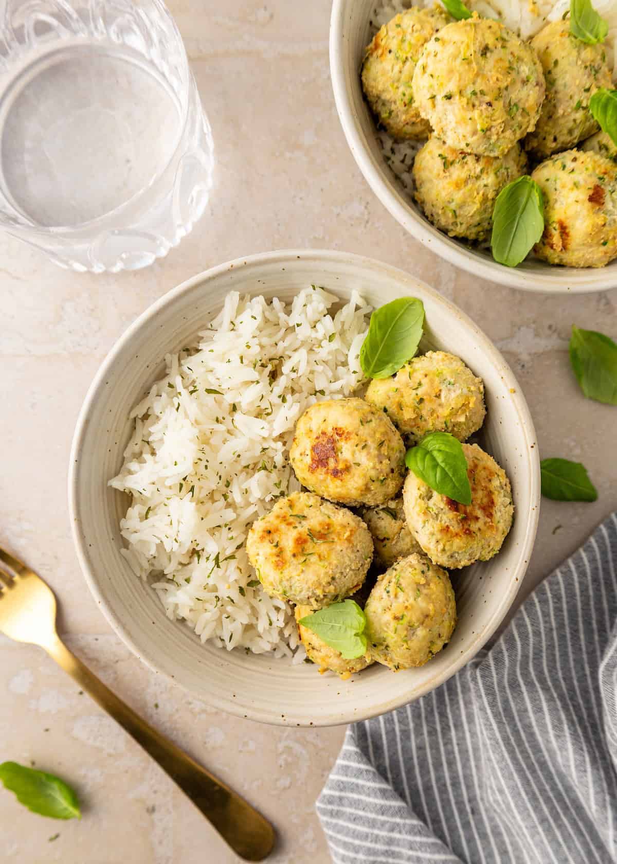 A bowl of rice topped with golden chicken meatballs, finished with fresh basil leaves.
