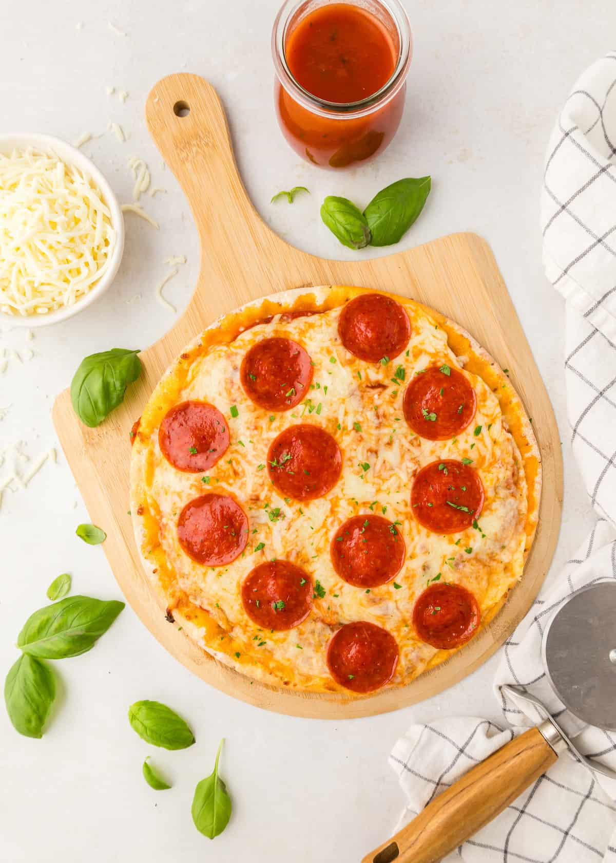 Cauliflower pizza on a wooden board with extra cheese, basil, and sauce.