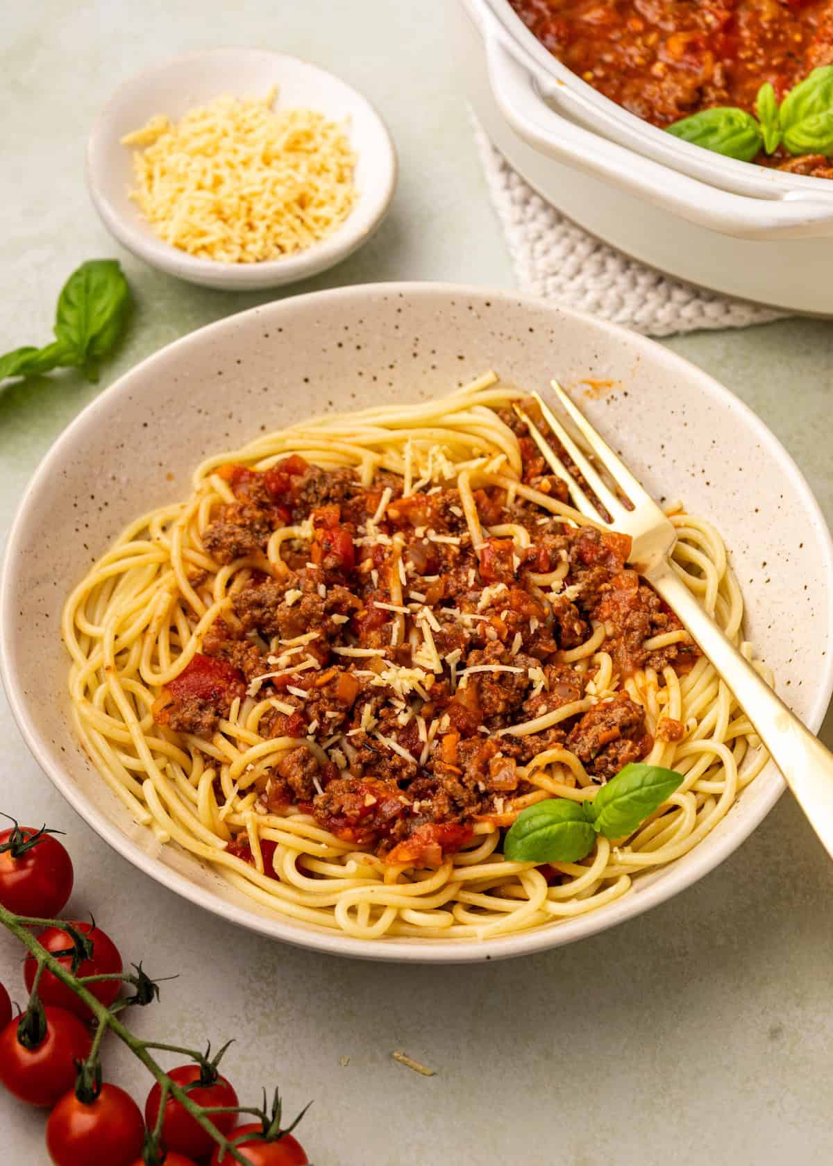 A bowl of spaghetti with homemade meat sauce, topped with cheese and basil, fork on the side.