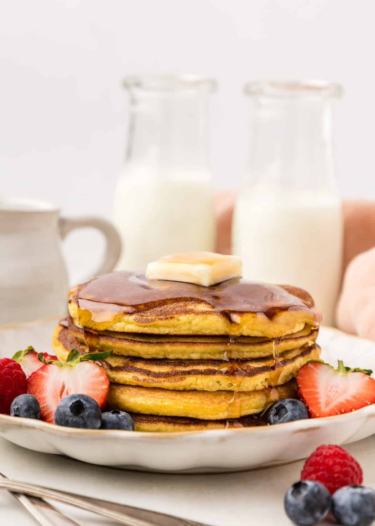 Coconut flour pancakes stacked, topped with syrup butter square and berries.