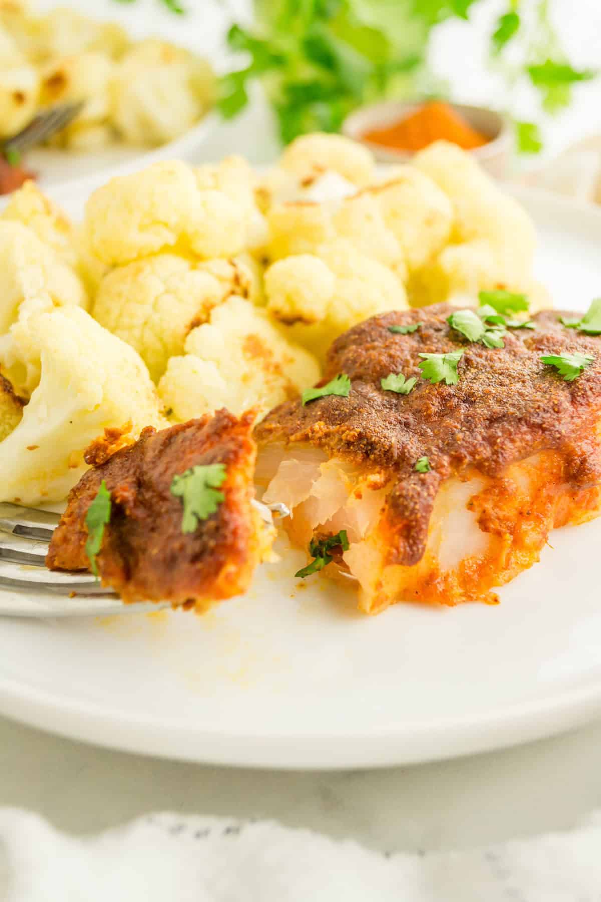 Tandoori Fish with red seasoning and cauliflower, garnished with herbs on a white plate.