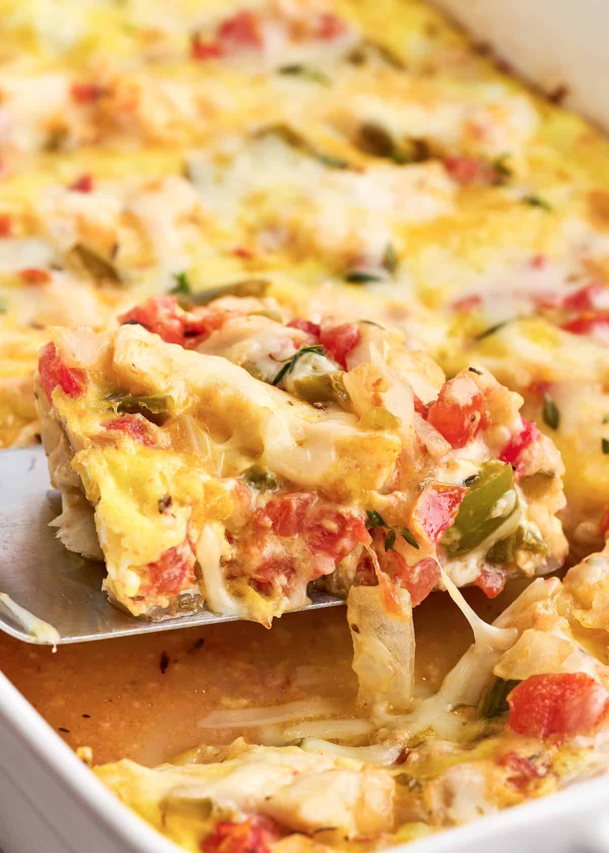 A cheesy Baked Haddock Casserole slice with tomatoes, peppers, and melted cheese being served.
