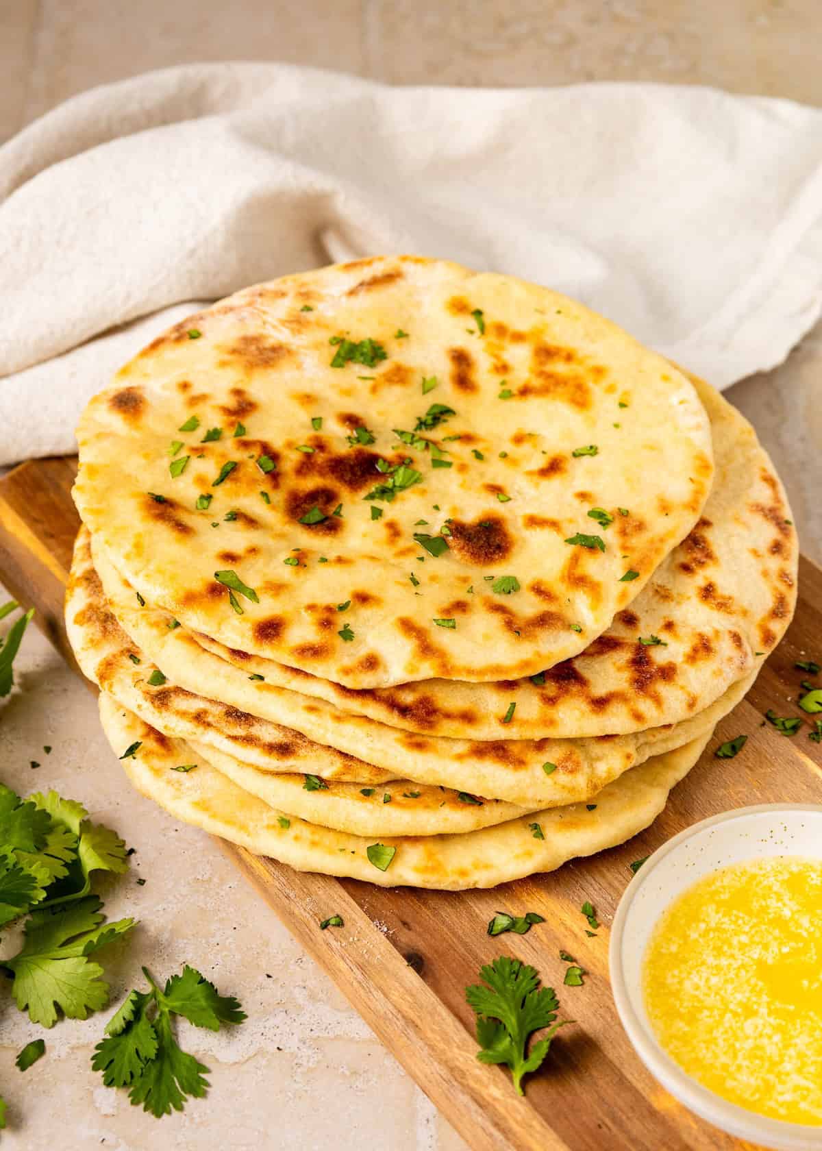 A stack of sourdough flatbread garnished with herbs beside a bowl of melted butter.