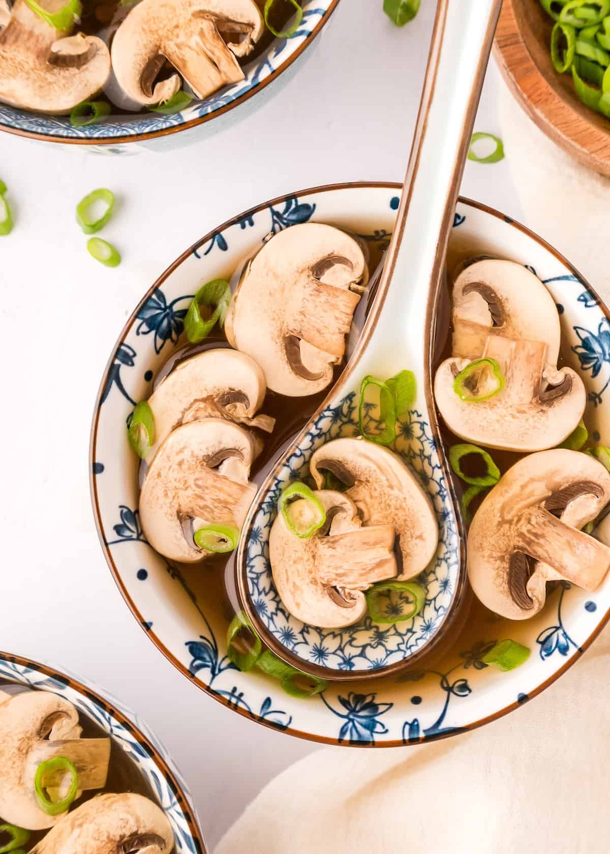 A bowl of Japanese clear onion soup with mushrooms, green onions, and a spoon.