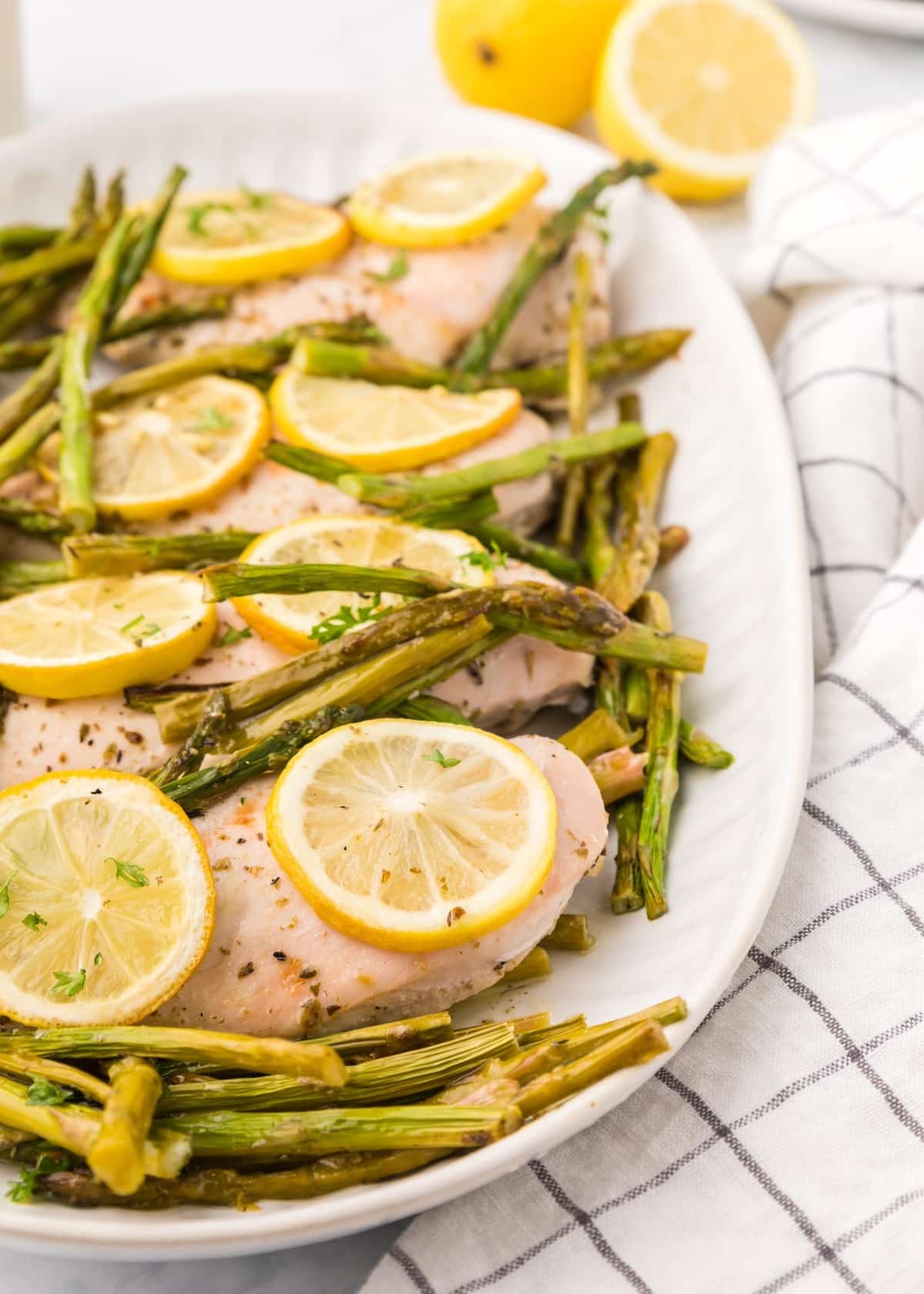Sheet Pan Lemon Chicken with asparagus and baked lemon slices on a white dish.