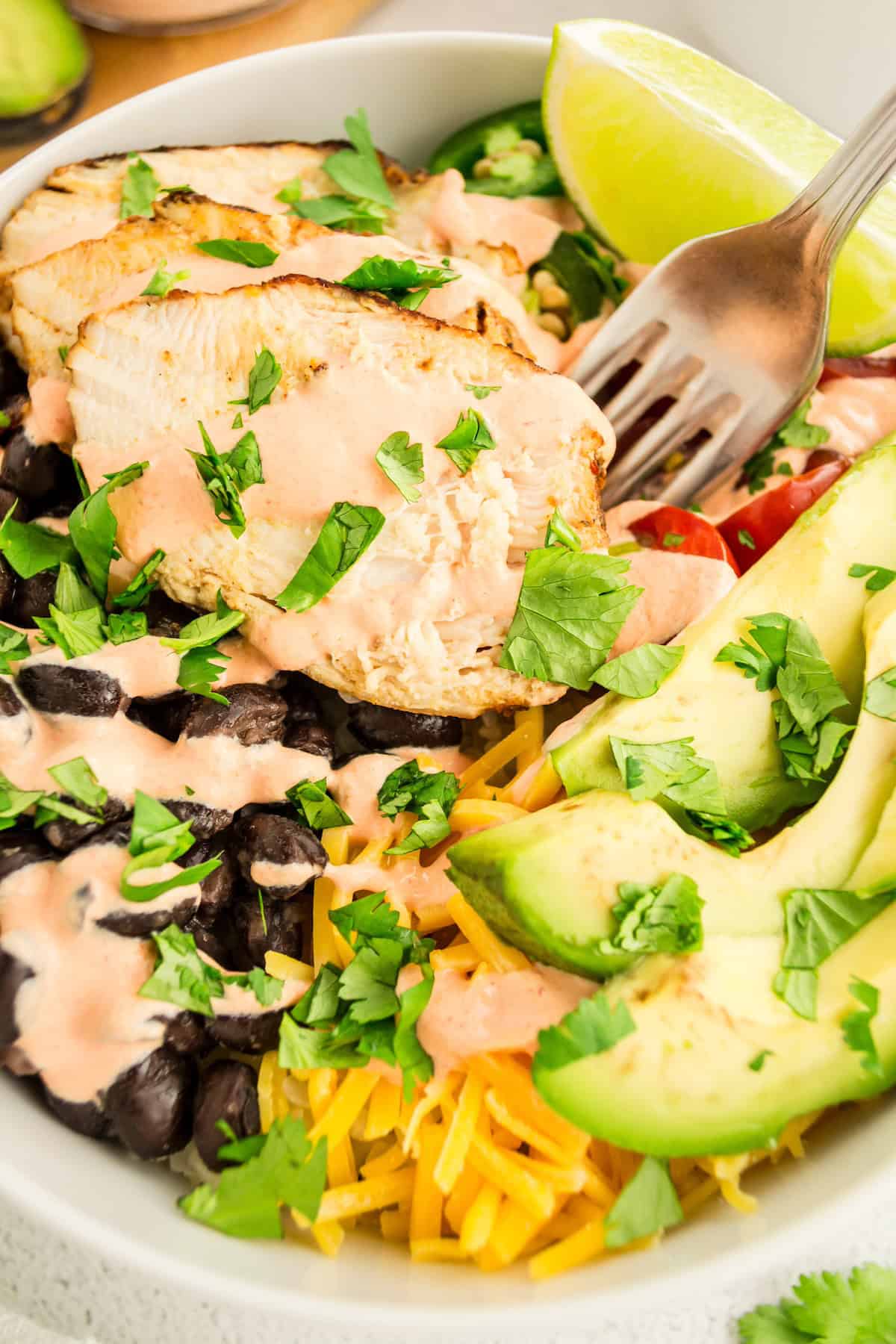 A Chicken Burrito Bowl with black beans, avocado, cheese, tomatoes, and lime.