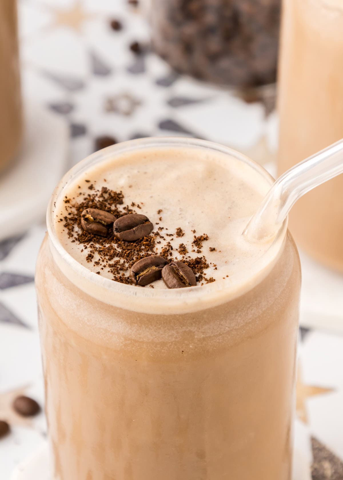 Iced coffee smoothie with foam, topped with beans and grounds, served with a clear straw.