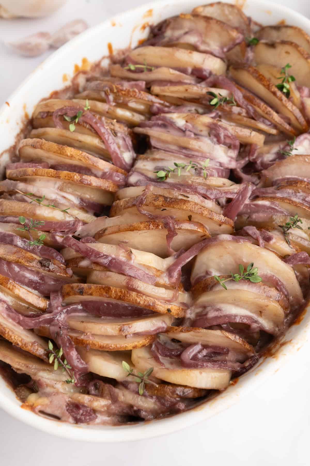 Sliced french onion potatoes baked with cheese and herbs, garnished with fresh thyme.