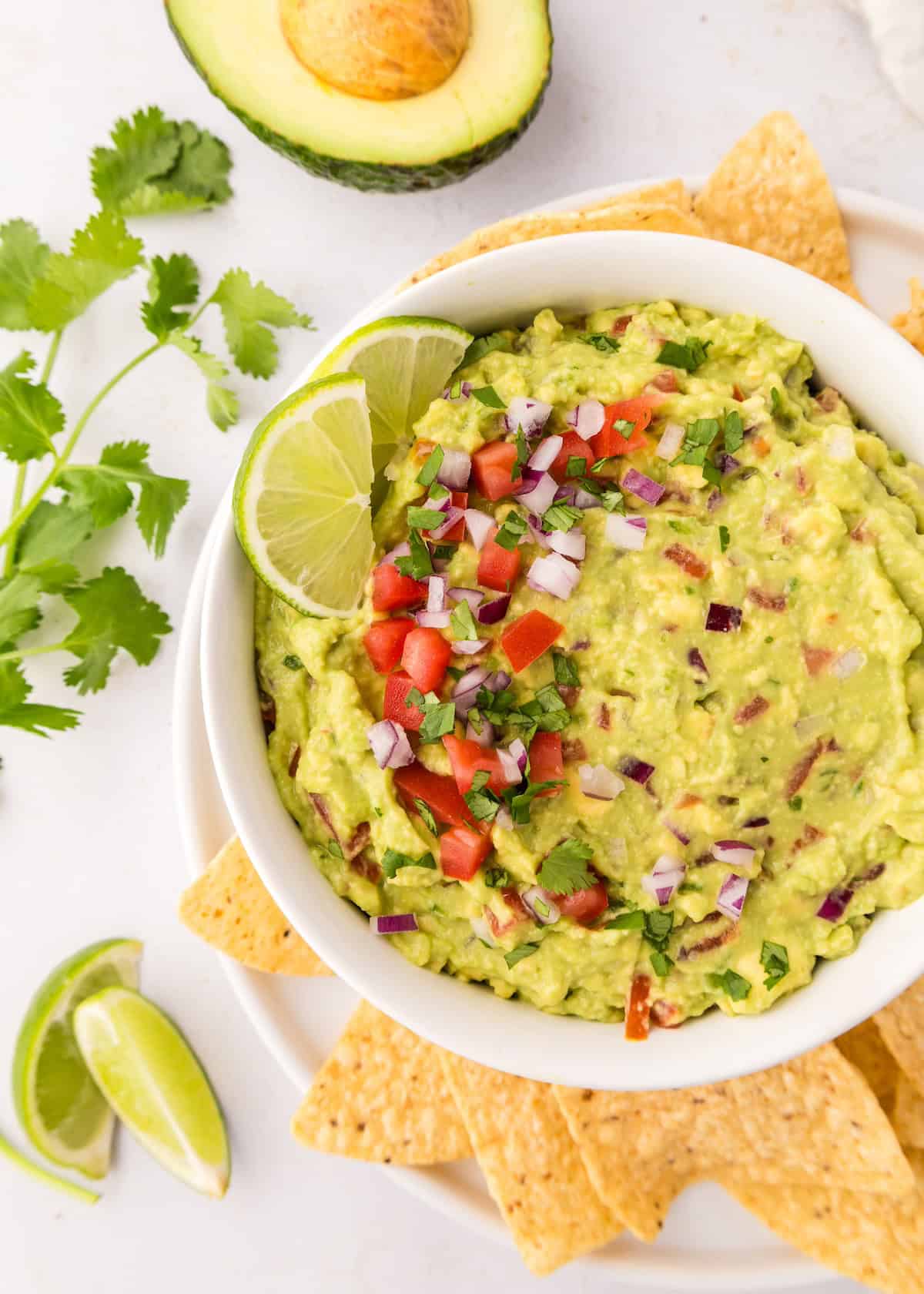 A bowl of guacamole topped with veggies, served with crispy tortilla chips.