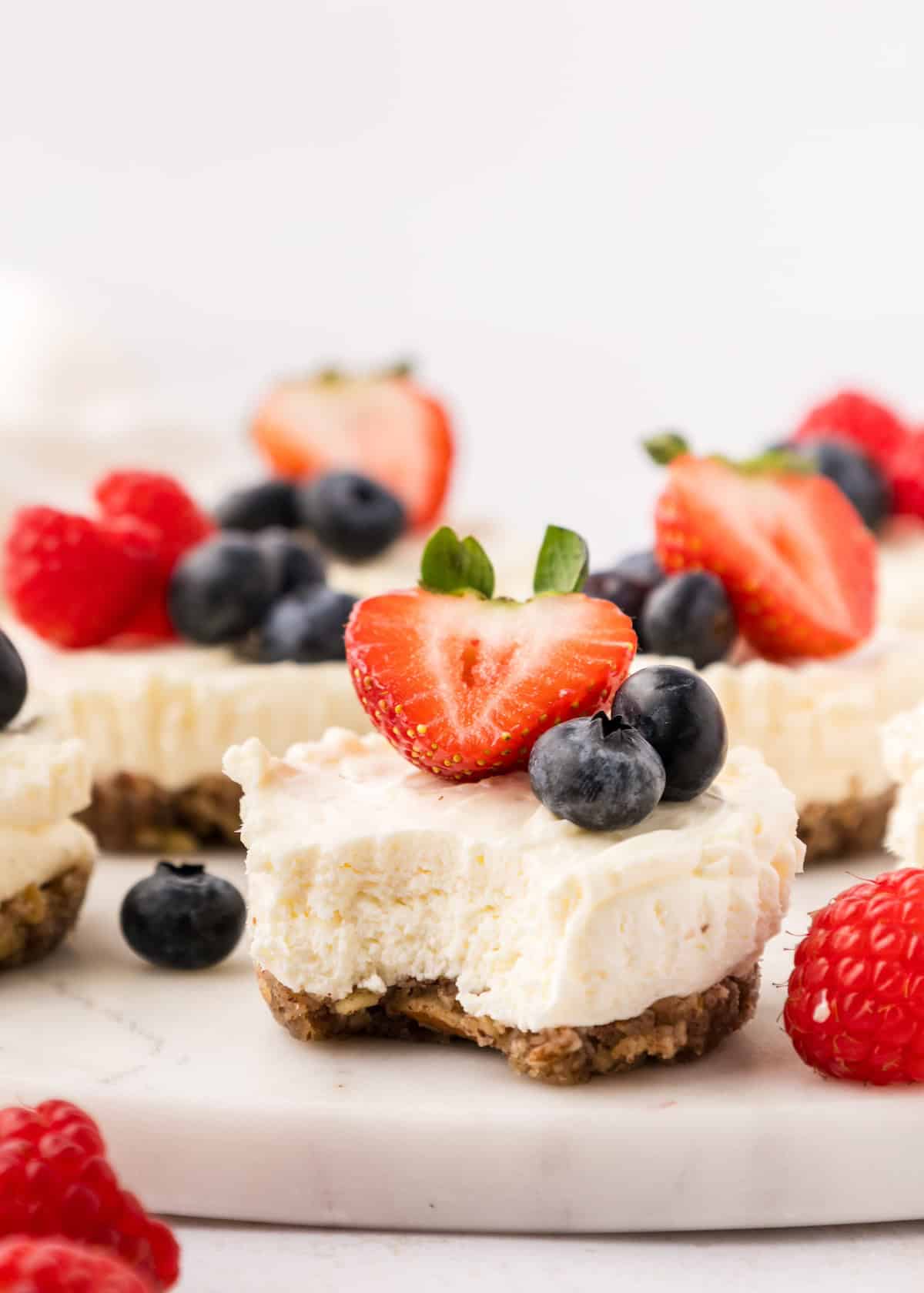 No Bake Mini Cheesecakes topped with strawberries and blueberries, with a bite taken out.