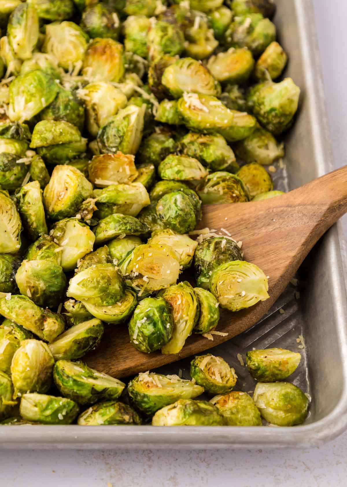 Parmesan Roasted Brussels Sprouts with grated cheese on a baking tray and wooden spatula.