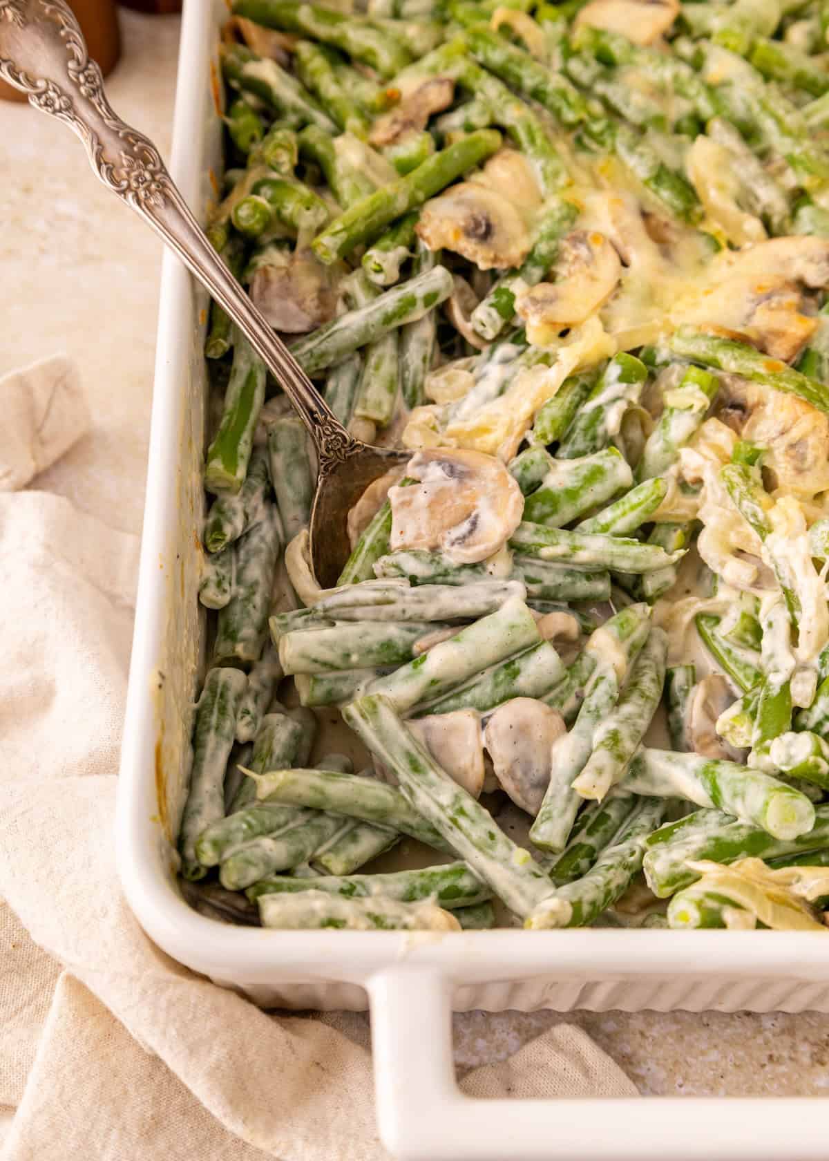 Green Bean Casserole with mushrooms and creamy sauce in a white baking dish with a spoon.