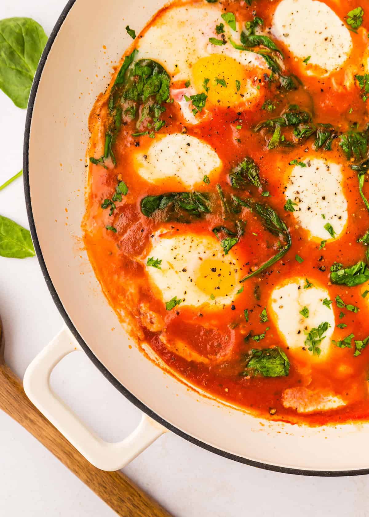 Italian eggs cooked in tomato sauce with spinach and herbs in a white pan.