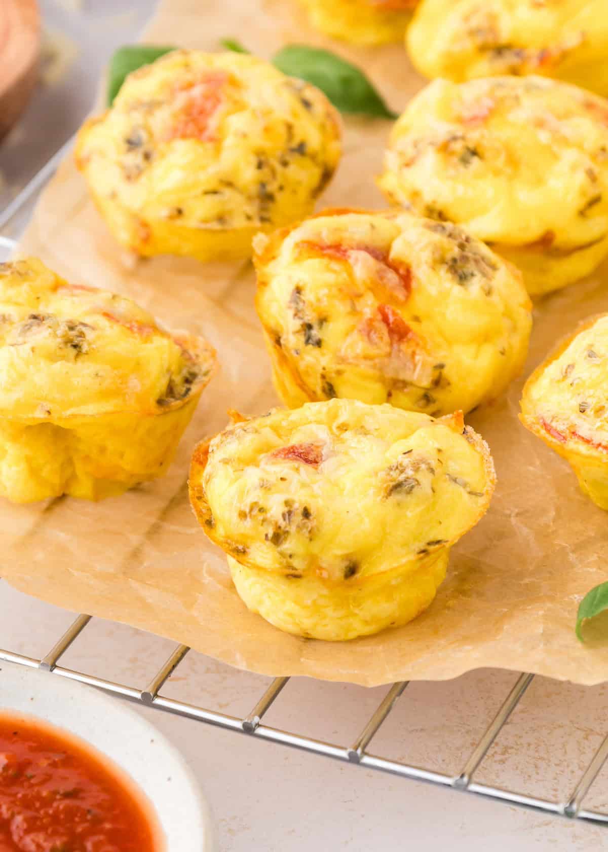 Mini pizza quiches with herbs and veggies on parchment paper, cooling on a wire rack.