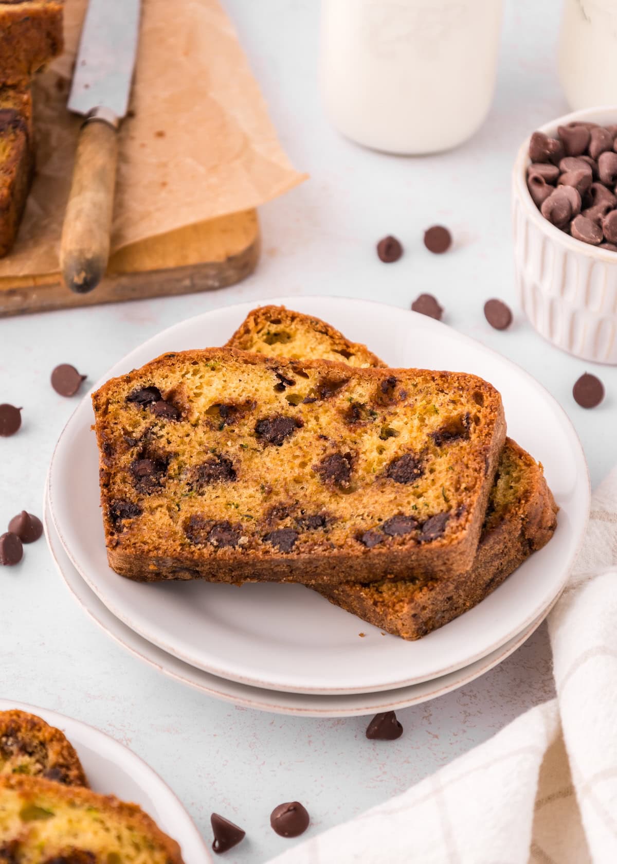 Two slices of Chocolate Chip Zucchini Bread on a white plate, with chocolate chips around.
