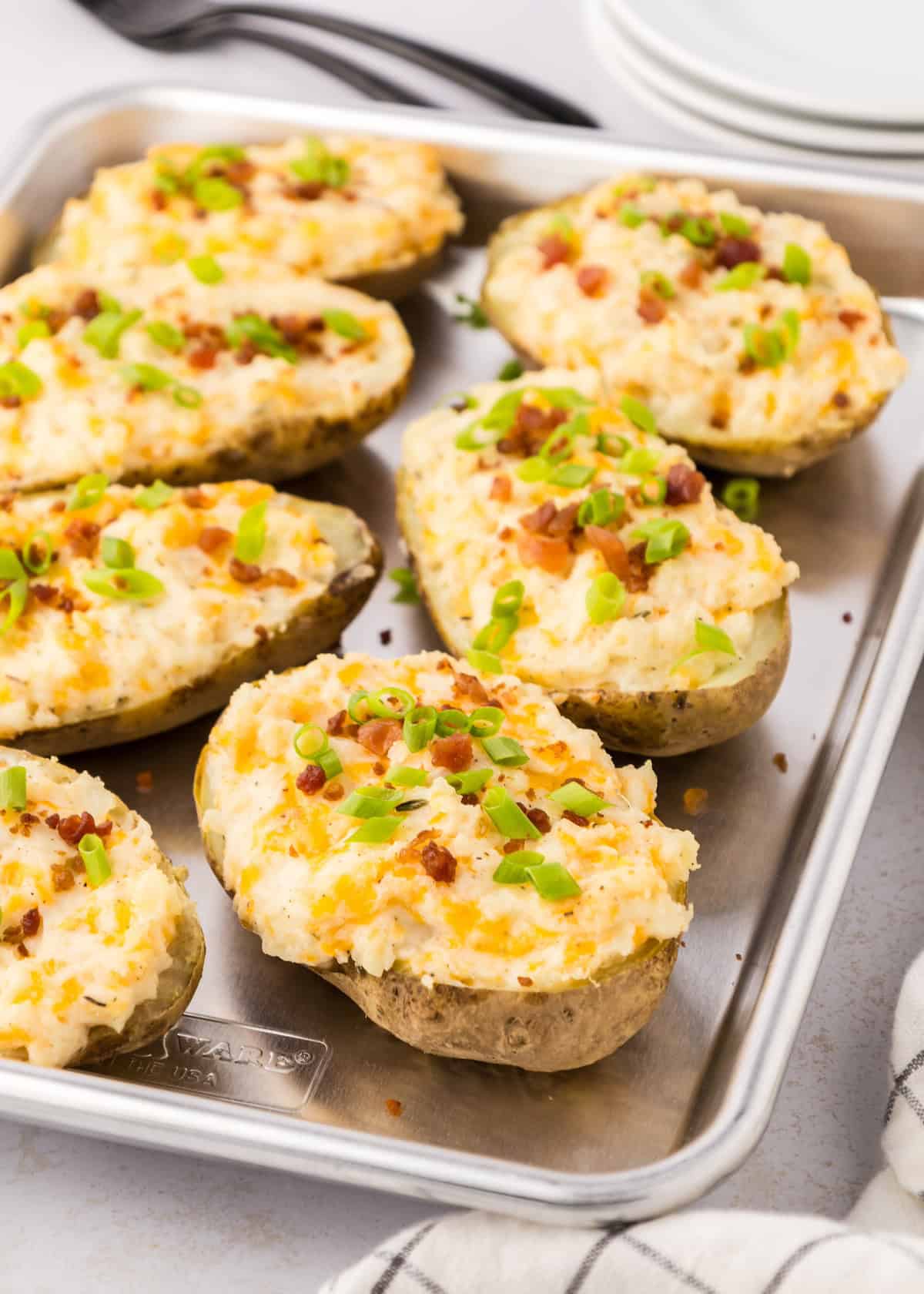 Twice baked potatoes halves filled with cheese, bacon bits, and green onions on a baking tray.