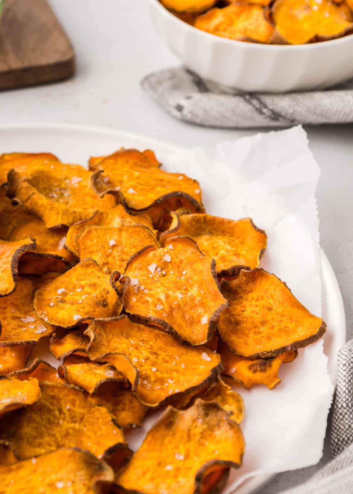Sweet Potato Chips served crispy and golden, sprinkled with salt on parchment-lined white plate.