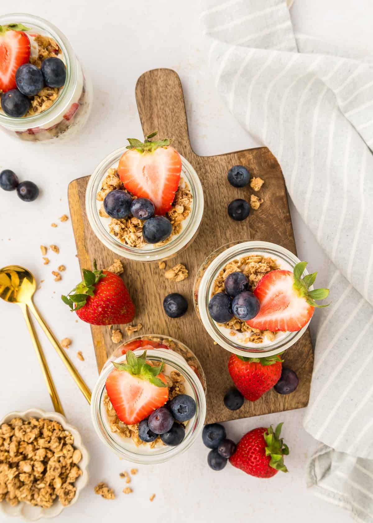 Yogurt Parfaits with granola, strawberries, and blueberries on a wooden board.