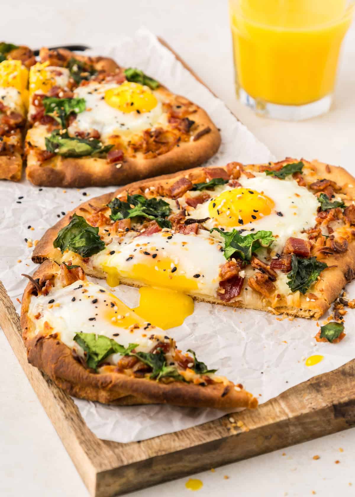 Breakfast flatbread served with orange juice, on a wooden cutting board.