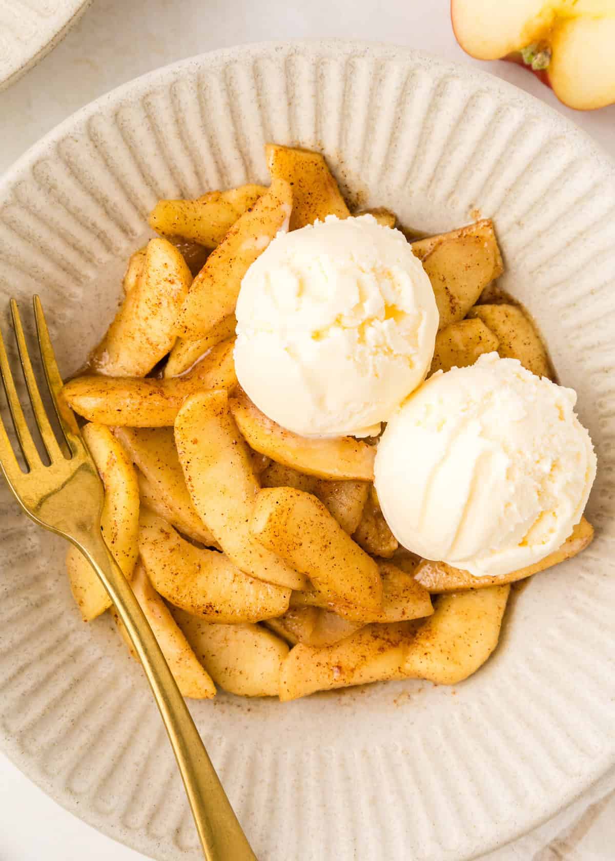Bowl of warm cinnamon apples topped with vanilla ice cream and a gold fork.