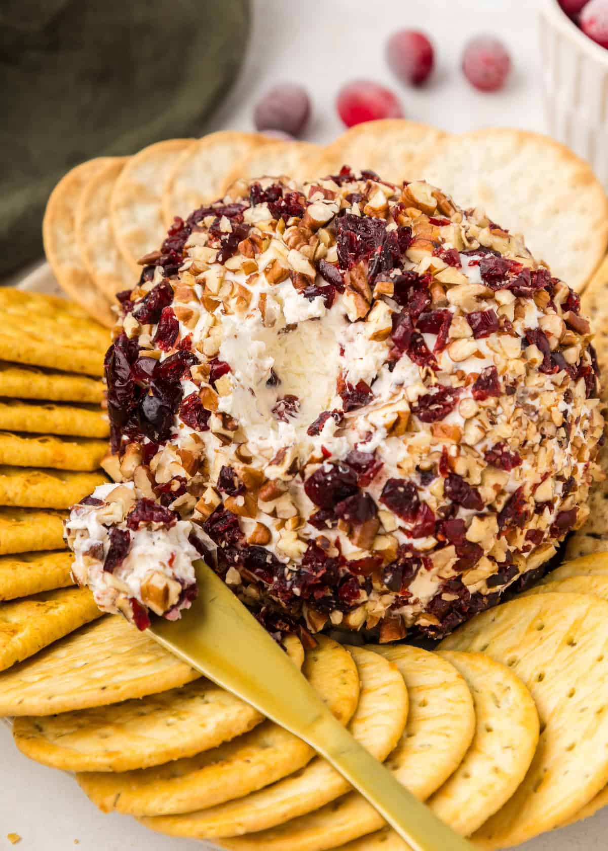 Cranberry pecan cheeseball served with crackers and spreading knife.