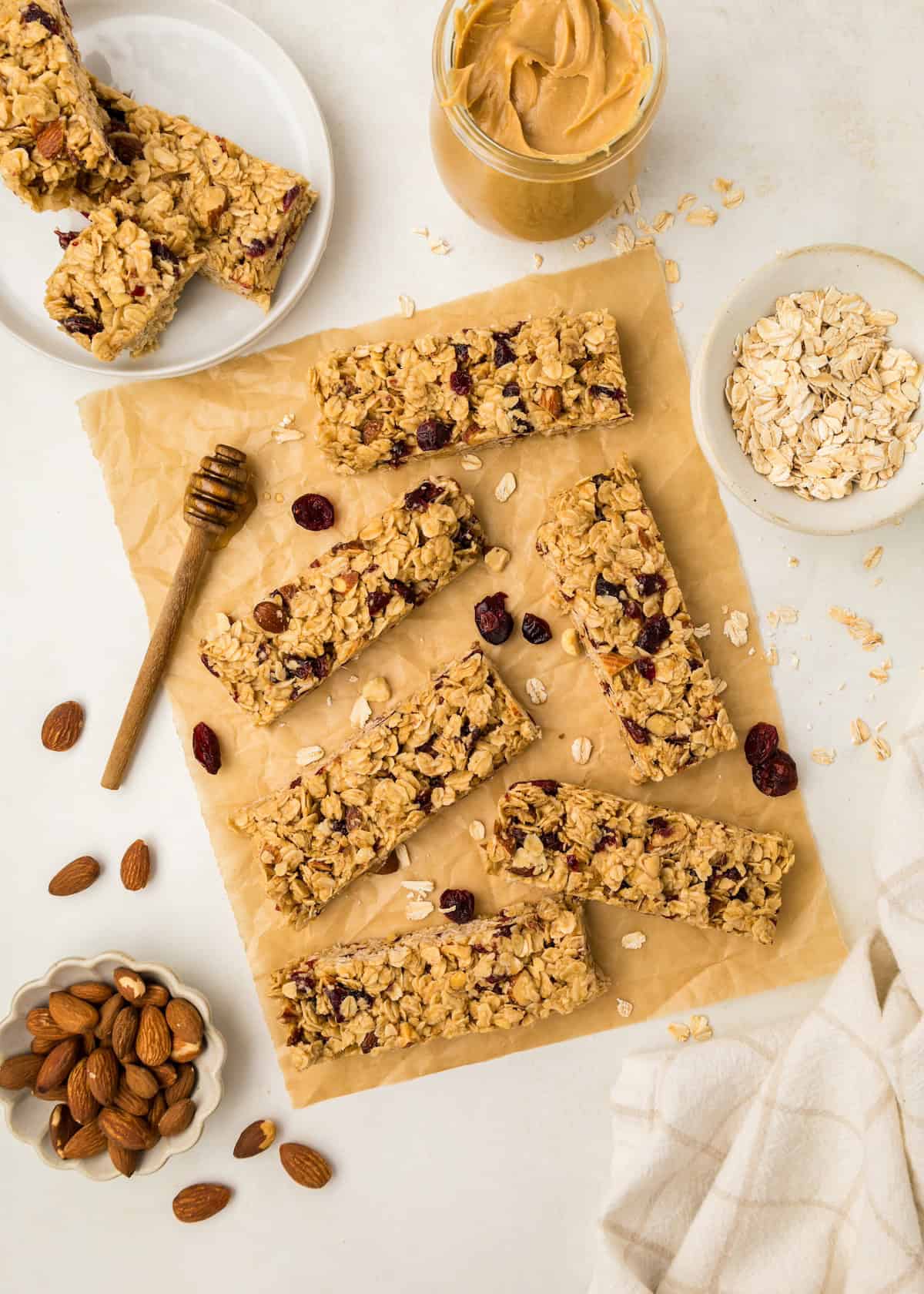 Breakfast Bars with oats, cranberries, and almonds on parchment with peanut butter and honey.