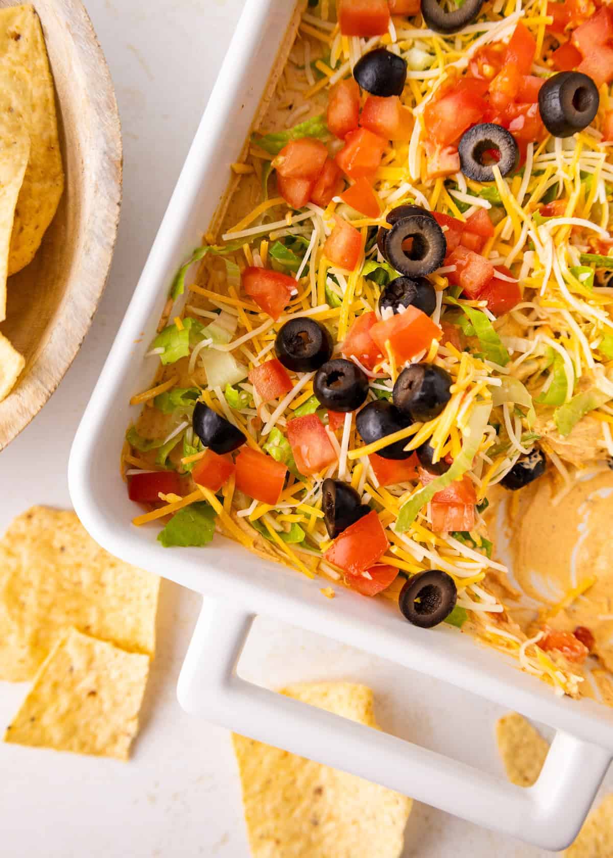 A casserole dish of layered Taco Dip with cheese, tomatoes, lettuce, and olives.