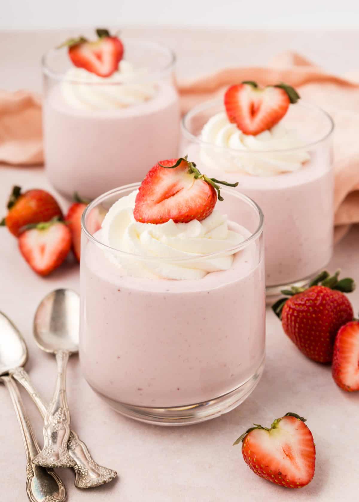 Three glasses of Strawberry Mousse topped with whipped cream and fresh strawberry slices.