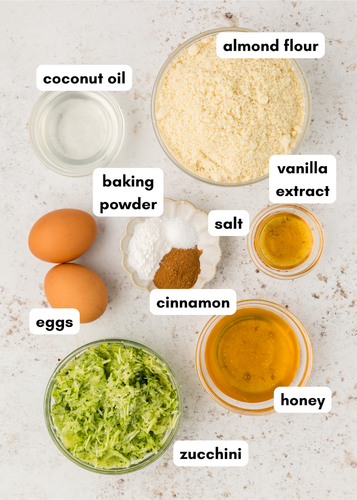 Baking ingredients for zucchini muffins: almond flour, eggs, honey, spices, oil, and extract.