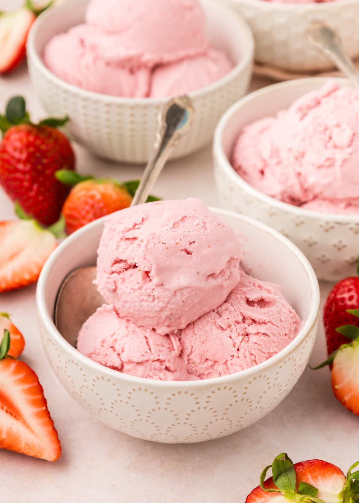 Bowl of strawberry frozen yogurt with a spoon, surrounded by fresh strawberries.