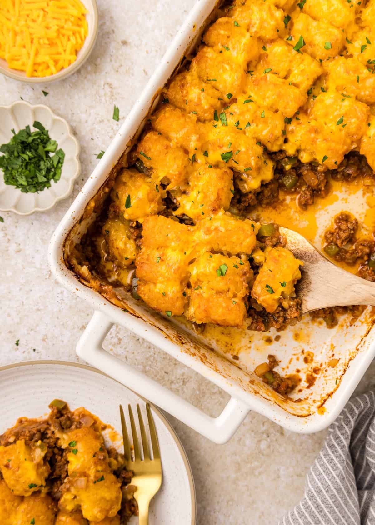 Sloppy Joe Casserole topped with tater tots, melted cheese, parsley, and shredded cheese.