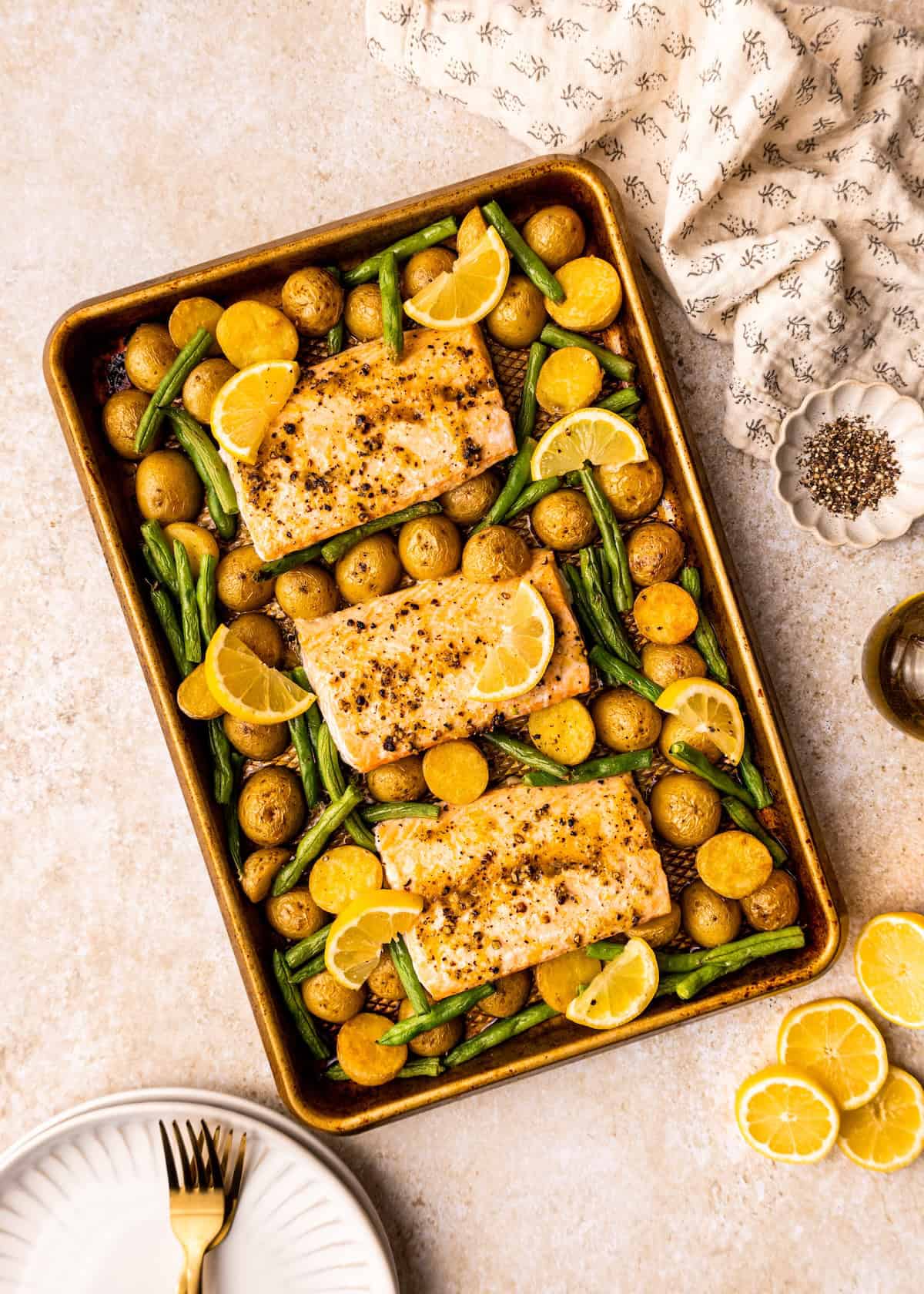 Sheet Pan Lemon Pepper Salmon with potatoes, green beans, and lemon slices on a light surface.