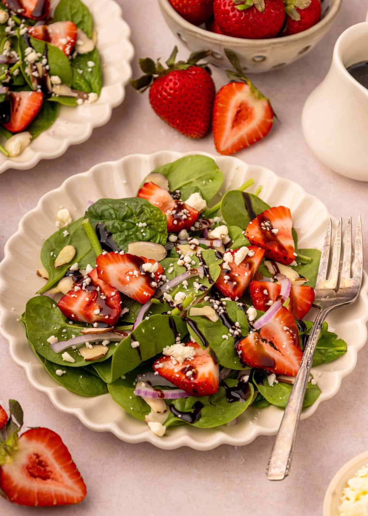 Strawberry spinach salad with feta, almonds, and balsamic drizzle on a white plate.