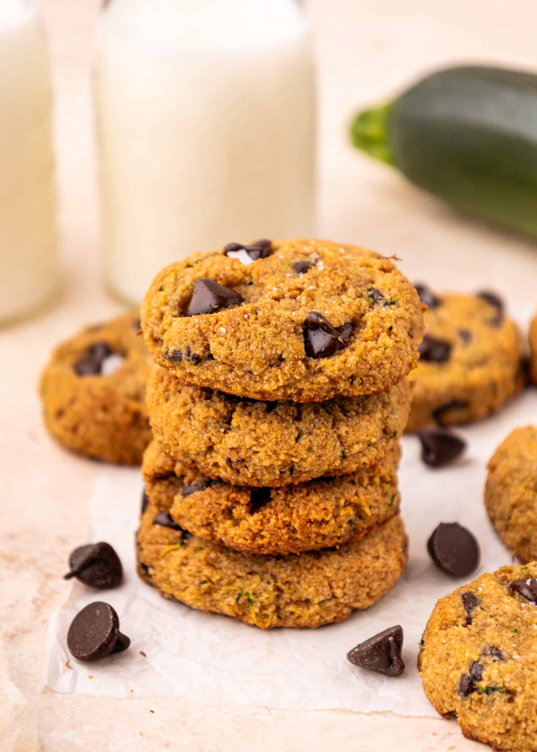 A stack of Chocolate Chip Zucchini Cookies with milk bottles and a zucchini in the background.