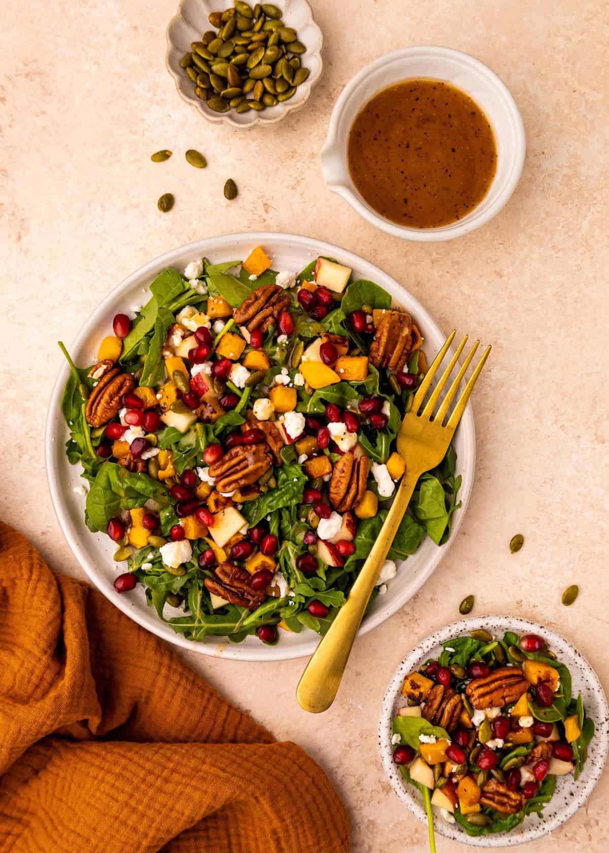 A Fall Harvest Salad with pecans, pomegranate, cheese, greens, and seeds on the side.