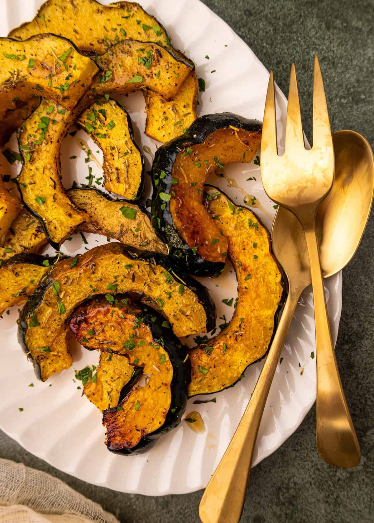 Roasted Acorn Squash slices served on a white plate with gold fork and spoon.