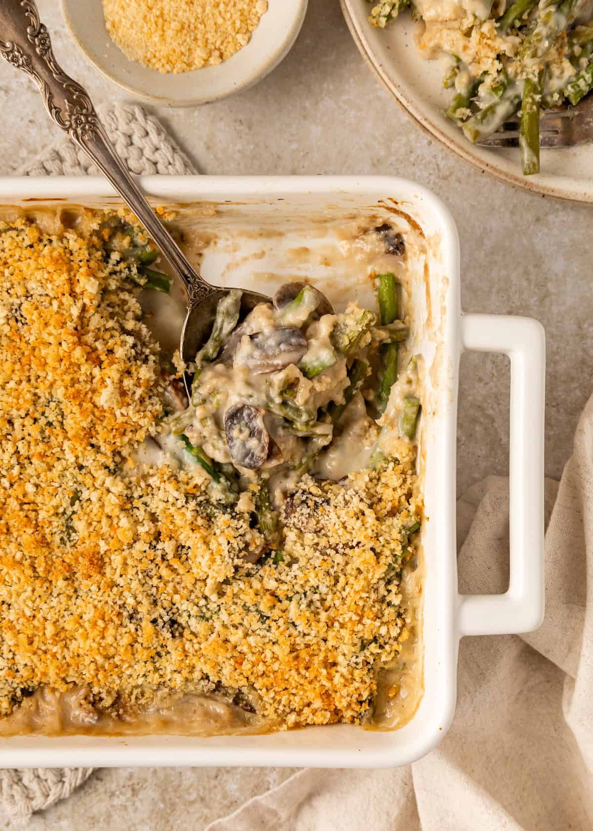 Casserole dish with creamy asparagus casserole topped with golden breadcrumbs and a serving spoon.