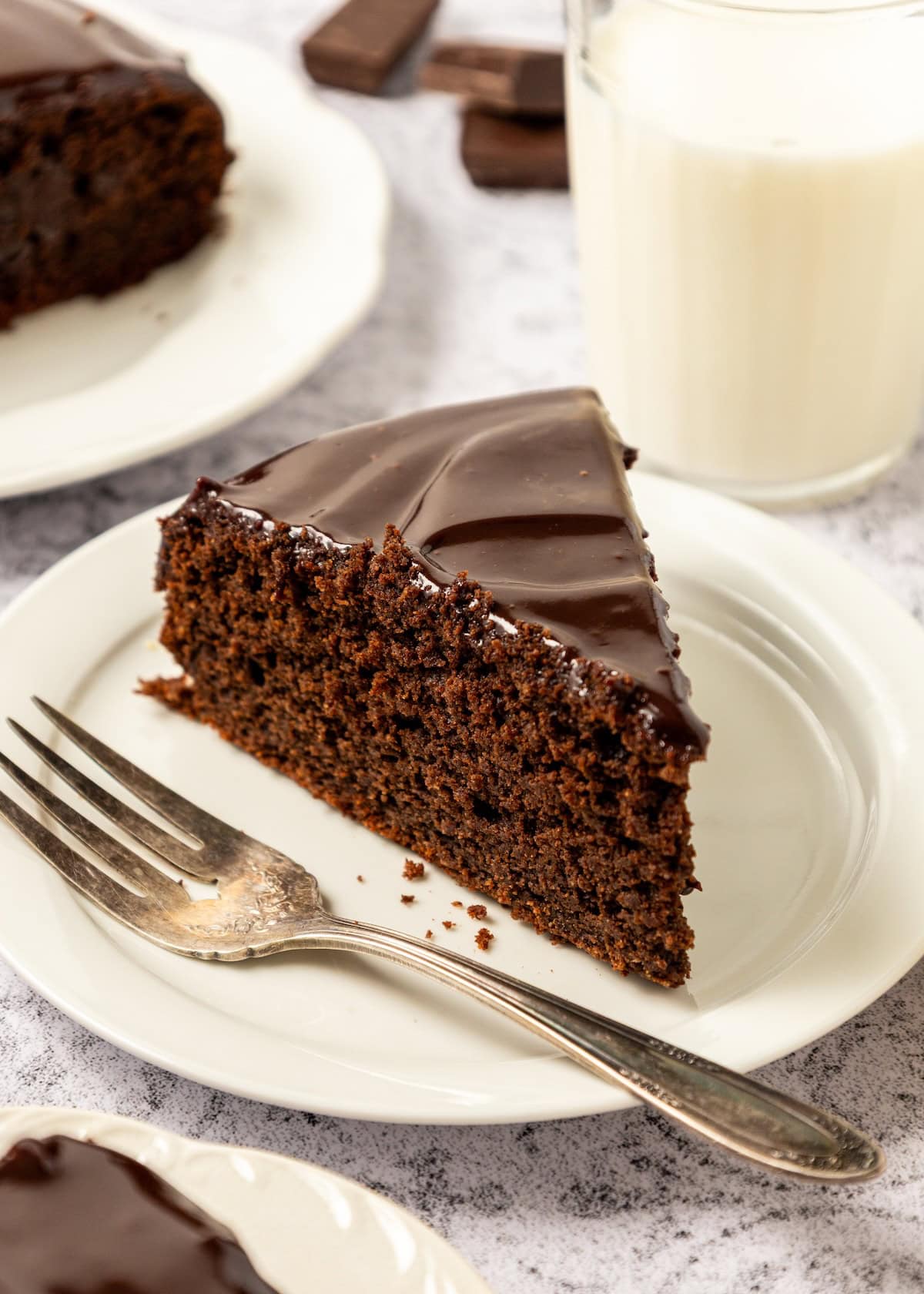 A slice of Chocolate Ricotta Cake on a small dish with a cup of milk.