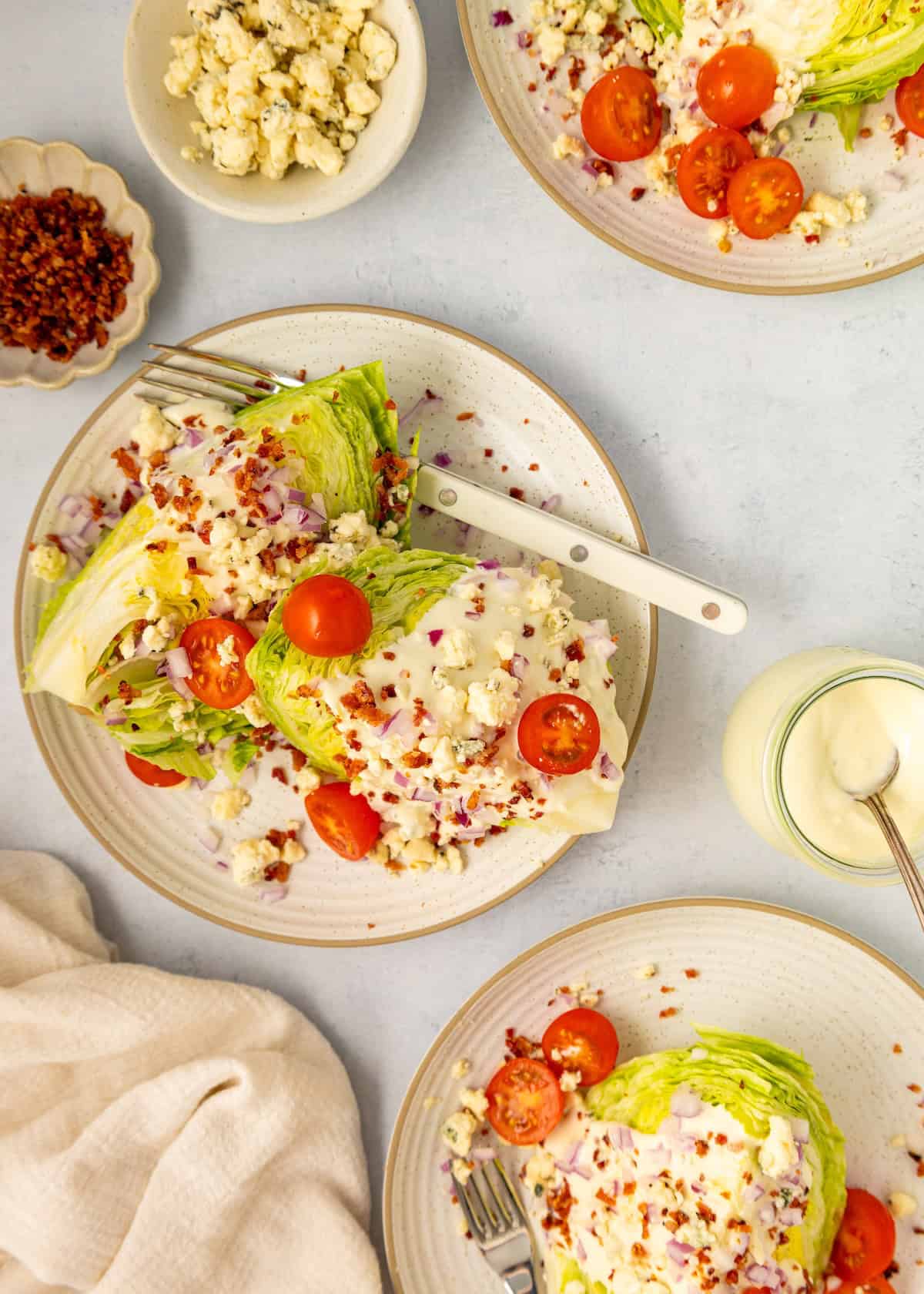 Plates of classic Wedge Salad with lettuce, tomatoes, blue cheese, bacon bits, and dressing.
