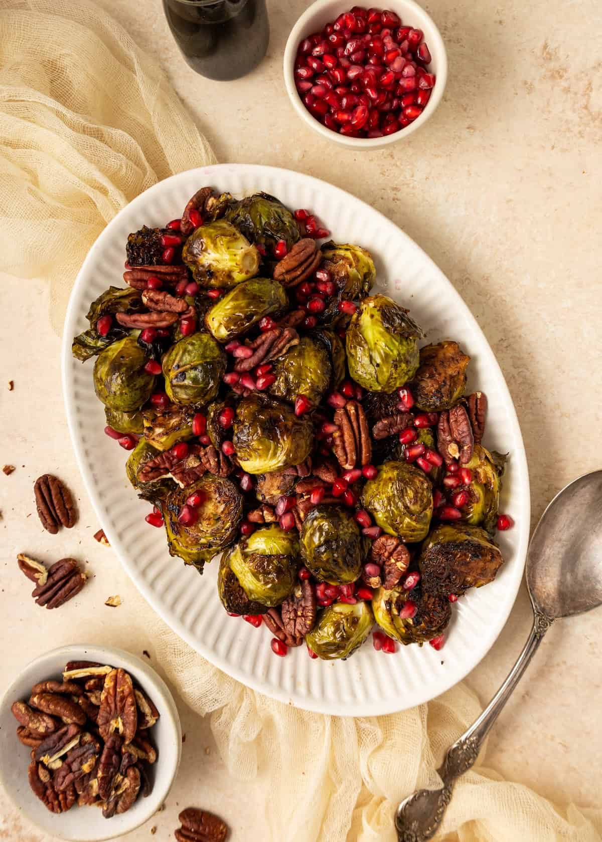 Balsamic Brussels Sprouts with pecans and pomegranate seeds on a white oval platter.